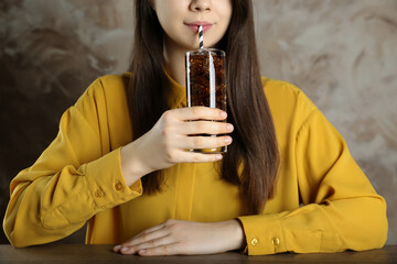 Woman drinking cola with ice at wooden table against grey background, closeup. Refreshing soda water
