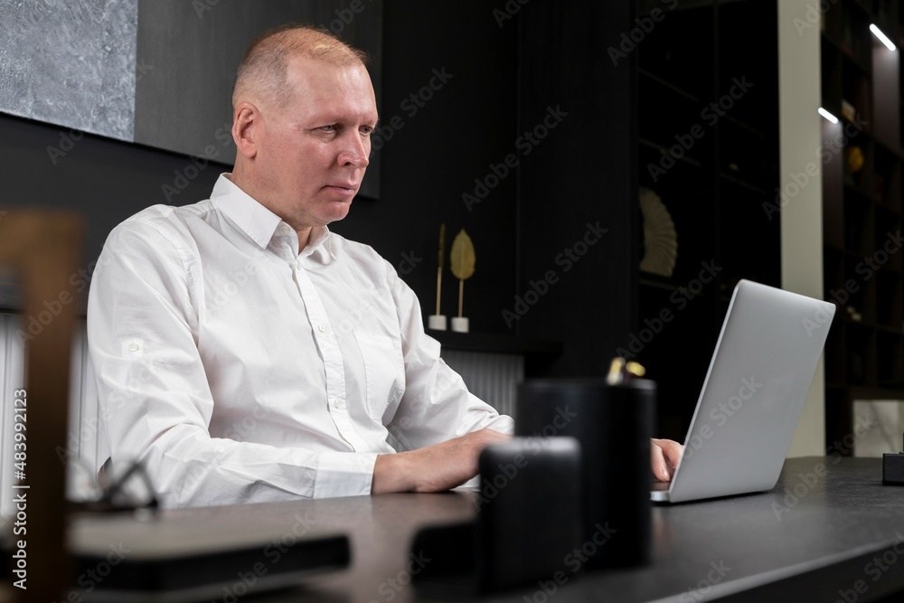Poster serious mature businessman in formal clothes sitting at desk and working on laptop in office. workin