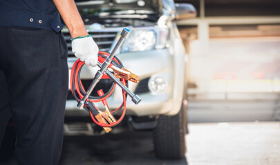 Auto mechanic holding vehicle maintenance equipment, battery charger and wheel wrench, with blur of...