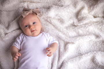 baby girl lying on a white blanket in white clothes on her stomach and smiling, looking at the camera, baby morning, baby stuff concept. place for text