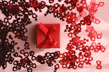 Small red giftbox and heart confetti on pale pink background. Flat lay. 