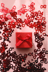 Small red giftbox and heart confetti on pale pink background. Flat lay. 
