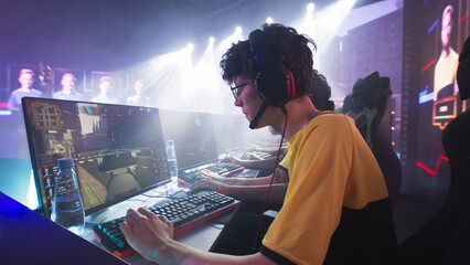Esportsman gamer in glasses and headphones playing shooter on computer near team while taking park in professional gaming championship battle © Framestock