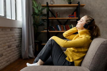 Beautiful pleased woman listening to music in headphones while sitting on sofa at home