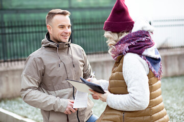 Portrait of two people dark-hared man and blonde hair woman back with documents holding pencil near house