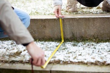 Cropped image of two people holding yellow coil roulette making measurements ground foundation of...