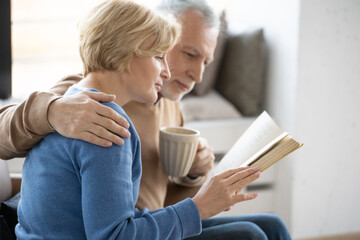 Embracing retired couple reading book together at home