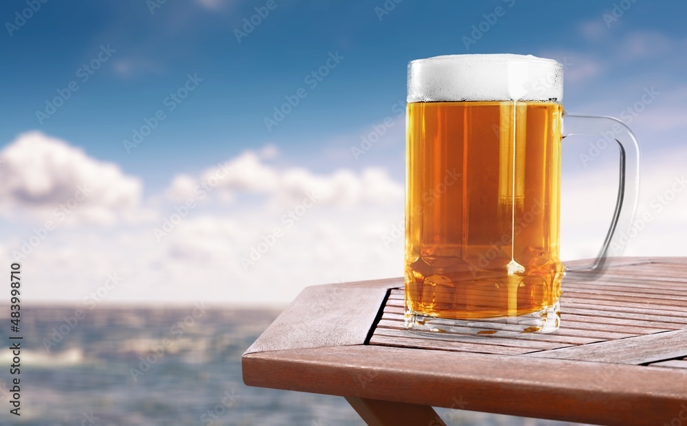 Canvas Prints A glass of beer with condensation on the wooden table. Blurred sparkling sea at the background. Summer vibes.