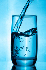 A jet of water is poured into a glass of clean water. A glass of water on a blue background into...