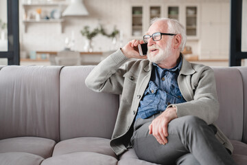 Smiling old elderly senior man grandfather talking on cellphone, communicating with grandchildren, e-banking, friends online on smart phone relaxing on the sofa