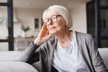 Sad tired ill sick lonely disappointed caucasian old elderly senior woman grandmother sitting on the sofa couch, feeling nostalgy, pain, missing grandchildren, bankruptcy, fraud at home - Powered by Adobe