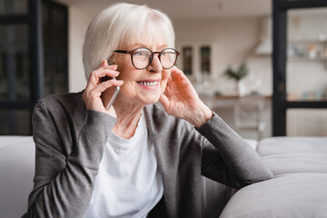 Happy smiling caucasian old senior elderly woman lady grandmother talking communicating with friends, grandchildren, colleagues on cellphone, smart phone online at home