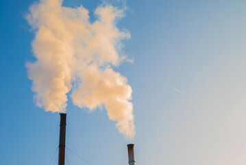 Two smoking factory chimneys and an airplane trail against a blue sky. Increase CO2 and greenhouse...