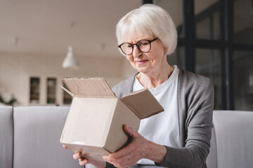 Angry sad disappointed elderly old senior woman grandmother opening wrong parcel, delivery post...