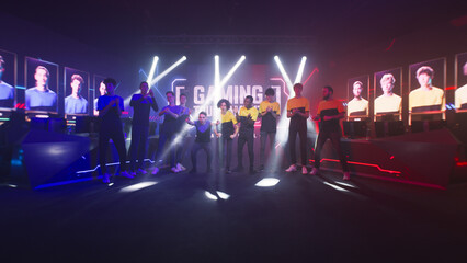 Group of teammates esport gamers walking and clapping hands then standing in front of monitor with gaming tournament banner at start of championship. - obrazy, fototapety, plakaty