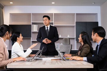 Adult Asian manager standing at the front of meeting room desk while listening his worker to explain about presentation and report. Teamwork brainstorm for office worker concept.