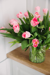 Fototapeta na wymiar Bouquet of pink tulips in a transparent vase on the kitchen table. International Women's Day 8 March. Selective focus.