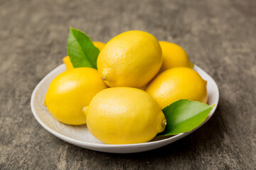 Fresh cutted lemon and whole lemons over round plate on colored background. Food and drink ingredients preparing. healthy eating theme top view vith copy space