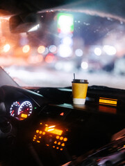 A glass of coffee is in the car against the backdrop of night city lights