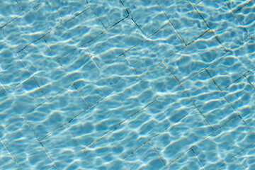 Beautiful texture of water with sun lights in a pool on the blue background of texture of small square ceramic tile