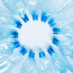 Crumpled blue plastic PET bottles lie in a circle with their necks in the center on a white...