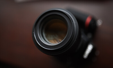 Photography as hobby. Close up view of the lens of a D-SLR camera against dark wood background.