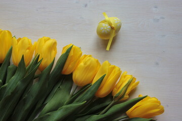 Yellow tulips and an Easter egg are lying on a light surface.