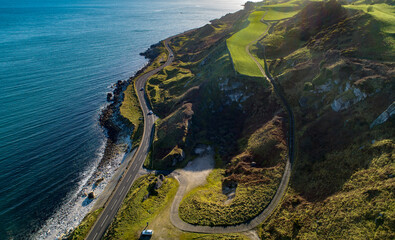 Northern Ireland. Atlantic coastline with famous coast road called Causeway Coastal Route and cliffs. One of the most scenic coastal roads in Europe. Aerial view in winter with cars against the sun - 484003341