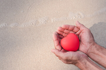 Men's hands hugging red hearts tenderly on beautiful sand, encouragement,world mental health day,sharing,organ or heart donation,14 February valentine, Love and save nature or protect the environment.