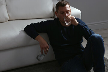 Fototapeta na wymiar Addicted man drinking alcohol near sofa indoors