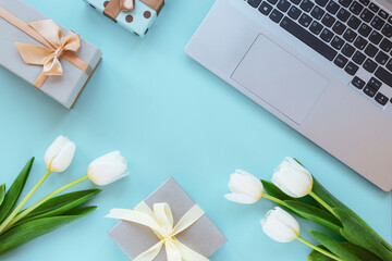 Laptop, gift boxes, tulip flowers on blue background. Spring holidays, online shopping concept. Top view, flat lay