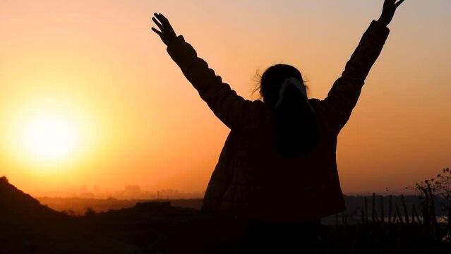 Silhouette of independent Indian woman raising her arms in front of the beautiful sunset. Female raising her arms while looking at the sunrise. Female enjoying beautiful evening and having fun