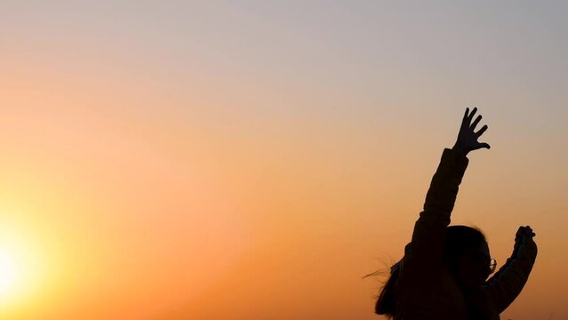 Silhouette of young happy Indian woman dancing and jumping. enjoying evening with raised hands at sunset. Carefree female at sunrise on mountain.  