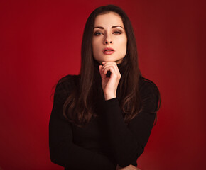 Beautiful confident serious business woman with red lipstick in black sweater posing on dark red background with empty copy space. Closeup