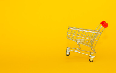 Metal basket for groceries from the supermarket on a yellow background. The concept of online...