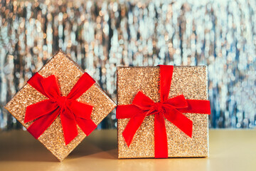 Glittering golden gift boxes with velvet red ribbon with a bow on the sparkling gold tinsel background. The concept of a gift for birthday, Valentine's day, Xmas, new year. Festive background.