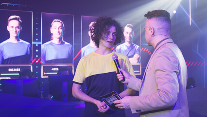 Young cyber sportsman smiling and speaking to adult male announcer while standing under neon illumination during gaming tournament © Framestock