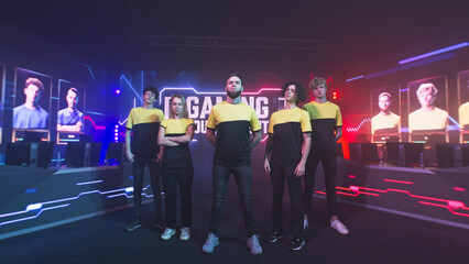 Assured team of teammates esportsman gamers in yellow uniform standing near bearded team leader and looking at camera during professional gaming competition © Framestock