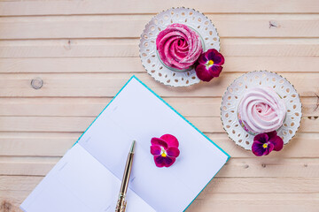Beautiful delicious dessert. Pink zephyr on wooden background and pink flowers.Plate with Berry,Meringue zephyr dessert. open diarz, book witj emptz pages.Goals, plans, morning