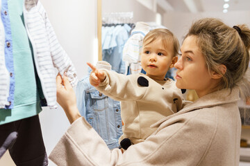 Woman with her baby son choosing clothing in clothes store