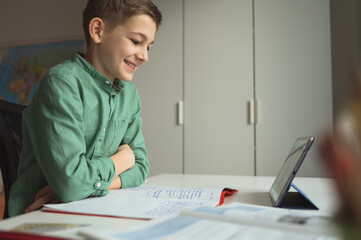 Smiling schoolboy chatting with his friends during online lesson