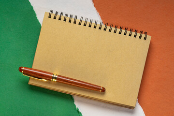 blank notebook against  paper abstract in colors of national flag of Ireland (green, white and orange), collection of handmade rag paper sheets