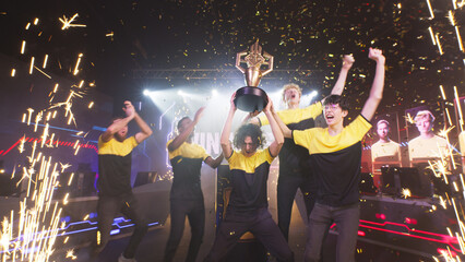 Cheerful diverse esports teammates gamers with golden cup screaming in excitement and celebrating victory in professional gaming championship under falling confetti © Framestock