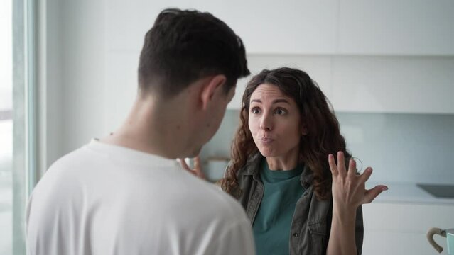 Married curly-haired woman quarrels angrily gesticulating and shouting with brunet husband over family problems standing in kitchen closeup