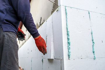 Construction worker installing styrofoam insulation sheets on house facade wall for thermal...