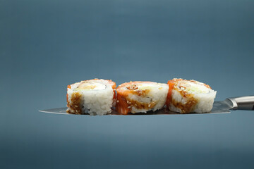 Philadelphia sushi with cheese and cucumbers on the blade of a knife