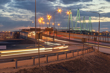 suspension bridge across the Neva River during heavy evening traffic with light paths from cars passing over the bridge