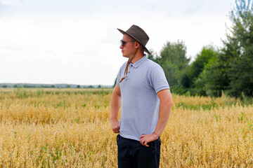 Naklejka na ściany i meble Crop and harvest. Portrait of farmer standing in gold wheat field with blue sky in background. Young man wearing sunglasses and cowboy hat in a field examining wheat crop. Oats analysis agronomist