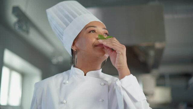 Black Female Chef Takes Fresh Herb, Enjoys Smell with a Smile, Secret Ingredient that Makes Grandmother's Recipe Special. Traditional Restaurant Kitchen with Authentic Dish, Healthy, Nurturing Food