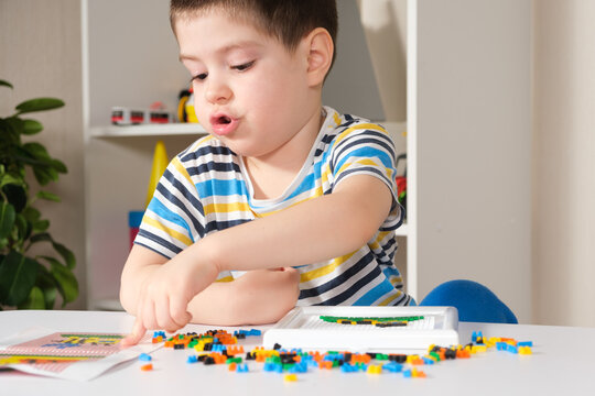A boy of 4 years old plays with a mosaic, collects a picture from small plastic parts. Development of fine motor skills in children